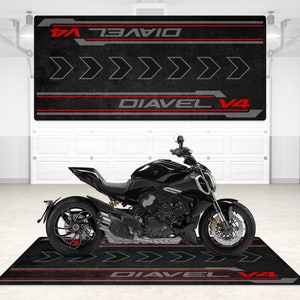 Op de afbeelding: Zwarte motorfiets met rode en grijze accenten op een zwarte en rode garagevloermat. De mat heeft de tekst "Diavel V4" erop gedrukt.