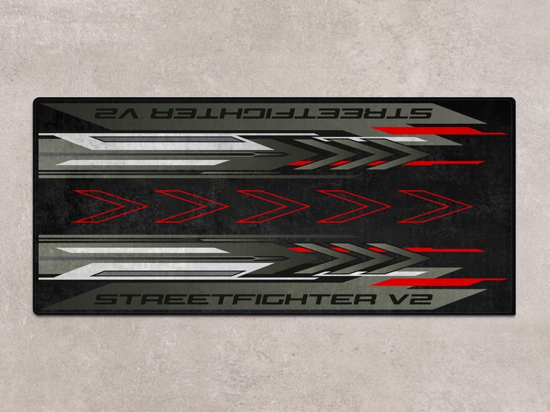 Puede incluir: Alfombrilla de rat&oacute;n negra y gris con un dise&ntilde;o rojo y blanco. El texto "STREET FIGHTER V2" est&aacute; impreso en la alfombrilla de rat&oacute;n.