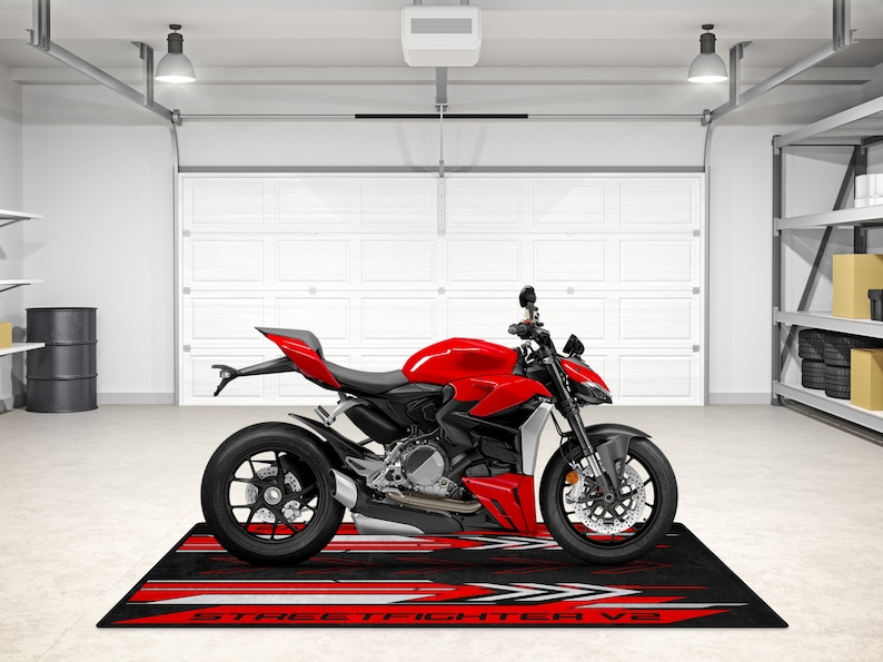 Puede incluir: Una motocicleta roja con ruedas negras y una alfombra de suelo con estampado negro y rojo con el texto "STREETFIGHTER V2".