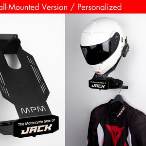 May include: A black metal motorcycle helmet and jacket storage rack with the text "MPM The Motorcycle Gear of JACK" on the front. The rack is mounted to a white wall.