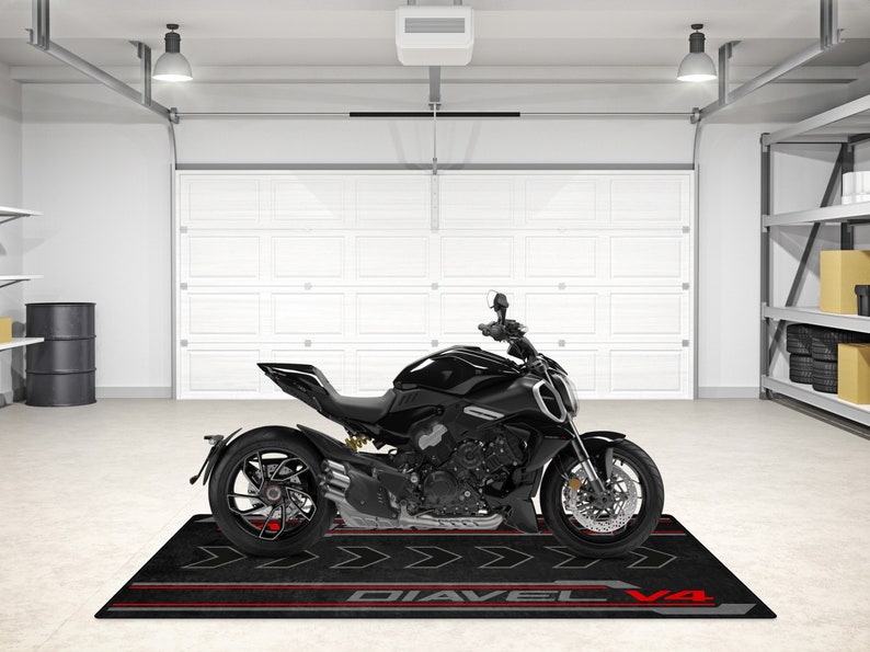 Op de afbeelding: Een zwarte motorfiets met rode accenten op de wielen en een zwarte mat met de tekst "Diavel V4" erop.