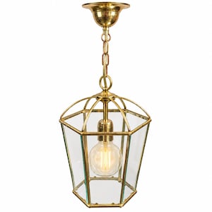 Peut inclure: Une suspension hexagonale dotée d'une structure en laiton poli et de panneaux en verre transparent. Cette lampe de style lanterne est suspendue par une chaîne et une rosace en laiton assorties, abritant une ampoule à filament visible.