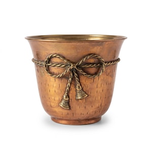 Cachepot de metal cor de cobre com laço de corda e borlas em tom de latão, textura martelada, floreira com borda alargada.