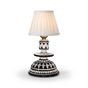 Puede incluir: Una lámpara de mesa con una pantalla de tela plisada blanca y una base de cerámica. La base está decorada con un patrón geométrico en blanco y negro, que incluye formas de diamante y líneas horizontales, con un casquillo de metal dorado.
