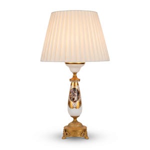 May include: A table lamp featuring a white pleated fabric shade atop a white and gold ceramic base. The base displays a central oval medallion with a painted scene, accented by gold filigree patterns and a decorative brass-toned metal pedestal.