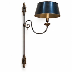 Puede incluir: Una lámpara de pared con un marco de metal en tono bronce oscuro con remates ornamentales en la parte superior e inferior. Un brazo curvo se extiende desde la barra vertical para sostener un casquillo y una pantalla cónica azul oscuro.