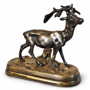 May include: A metallic bronze-toned deer figurine standing on a textured, gold-coloured oval base. The deer features detailed antlers and a smooth, weathered finish, positioned as if walking across a small, uneven terrain element on the base.