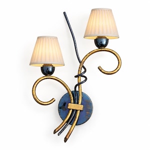 May include: A two-light wall sconce featuring a circular dark blue base with gold and black curved metal arms. Two off-white pleated fabric shades are positioned at the ends of the arms, each supported by a dark blue spherical mount.
