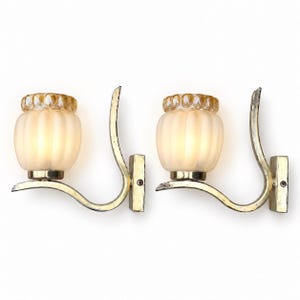 May include: A pair of wall sconces featuring curved metallic arms with a weathered finish. Each fixture holds a frosted, ribbed glass shade topped with a clear, textured amber glass rim, creating a distinct layered appearance for wall lighting.