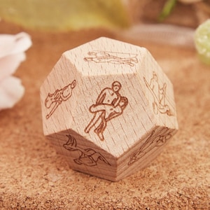 May include: An eight-sided wooden dice, with each side featuring a different illustration of a couple in a romantic pose. The dice is made from light brown wood and has a natural finish.