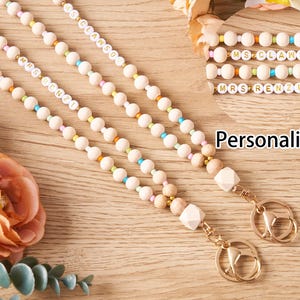 Pode incluir: Cord&otilde;es personalizados com contas de madeira, detalhes coloridos e ferragens douradas. Os cord&otilde;es apresentam nomes como "MRS RENZI" e "MS CLAWSON" em contas de letras brancas. O fundo inclui flores e a palavra "Personalized".