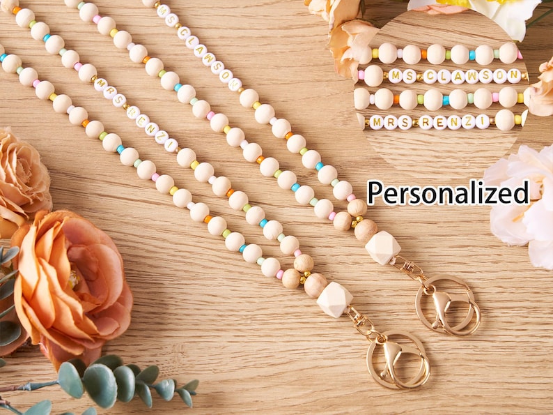 Pode incluir: Cord&otilde;es personalizados com contas de madeira, detalhes coloridos e ferragens douradas. Os cord&otilde;es apresentam nomes como "MRS RENZI" e "MS CLAWSON" em contas de letras brancas. O fundo inclui flores e a palavra "Personalized".