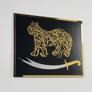 Puede incluir: Una pieza de arte de pared enmarcada en negro con un dise&ntilde;o caligr&aacute;fico dorado de un le&oacute;n y una espada plateada. El le&oacute;n est&aacute; mirando hacia la derecha y la espada est&aacute; curvada.