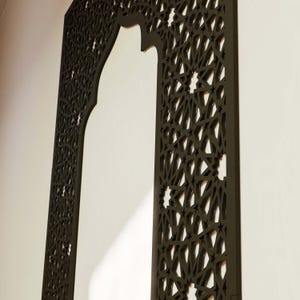 May include: A dark brown, intricately carved wooden decorative panel. The panel features a Moorish arch design with geometric star and diamond patterns. The panel is mounted on a white wall, creating a contrast.