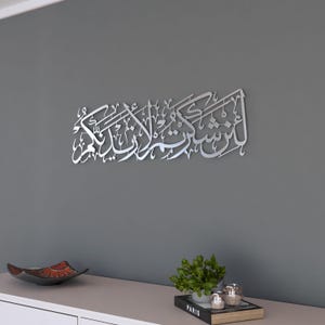 May include: Silver metal wall art featuring Arabic calligraphy. The calligraphy reads "In the name of Allah, the Most Gracious, the Most Merciful".