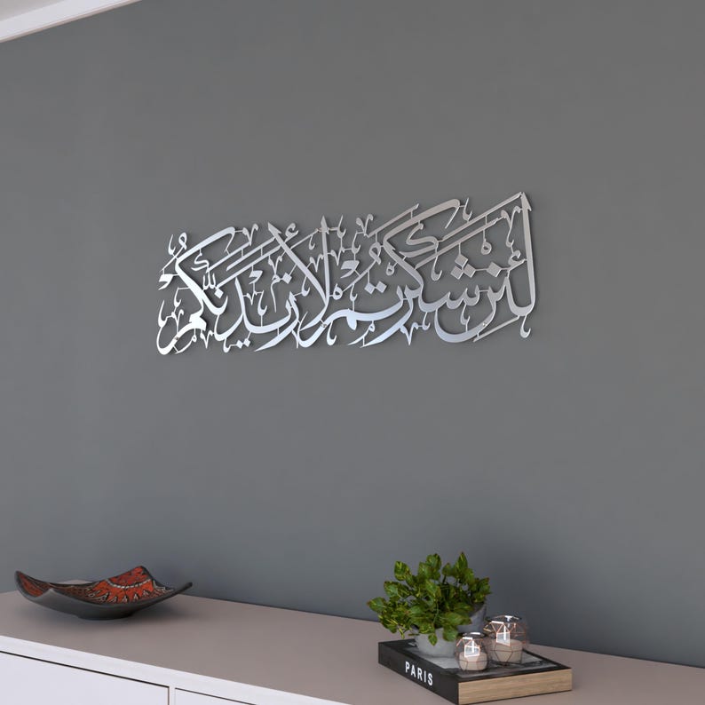May include: Silver metal wall art featuring Arabic calligraphy. The calligraphy reads "In the name of Allah, the Most Gracious, the Most Merciful".
