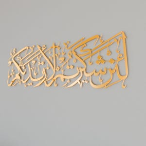 May include: Gold Arabic calligraphy wall art with intricate lettering. The text reads "Subhana-alladhi sakh-khara-lana hadha wa ma kunna lahu muqrinin wa inna ila Rabbi-na la munqalibun".