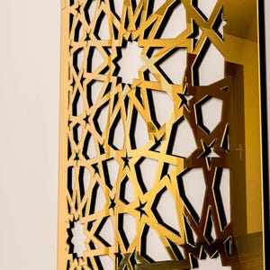 May include: A gold geometric wall panel featuring a repeating star and angular design. The panel is mounted on a white wall, creating a contrast with the gold. The design is intricate and detailed, with a modern aesthetic.