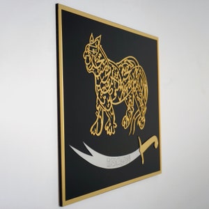 Puede incluir: Una pieza de arte de pared enmarcada en negro con un recorte dorado de un le&oacute;n con caligraf&iacute;a &aacute;rabe. Un cimitarra plateado con la palabra "Sayyid" en caligraf&iacute;a &aacute;rabe est&aacute; debajo del le&oacute;n.