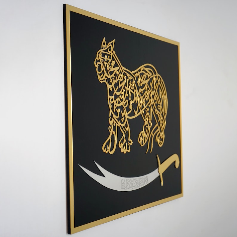 Puede incluir: Una pieza de arte de pared enmarcada en negro con un recorte dorado de un le&oacute;n con caligraf&iacute;a &aacute;rabe. Un cimitarra plateado con la palabra "Sayyid" en caligraf&iacute;a &aacute;rabe est&aacute; debajo del le&oacute;n.