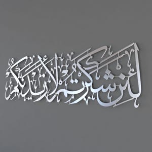 May include: Silver metal wall art featuring Arabic calligraphy. The text reads "In the name of Allah, the Most Gracious, the Most Merciful."