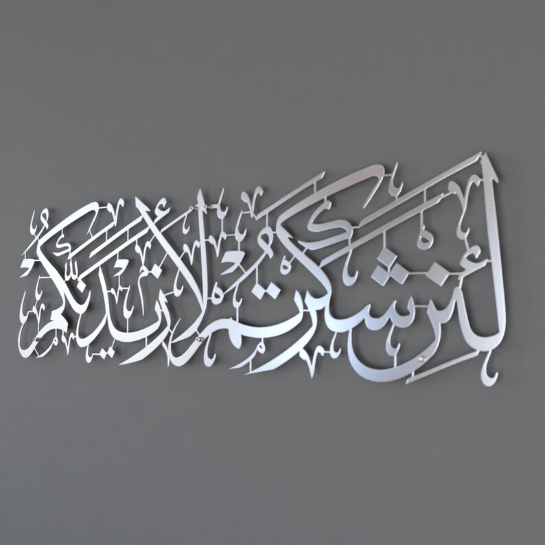 May include: Silver metal wall art featuring Arabic calligraphy. The text reads "In the name of Allah, the Most Gracious, the Most Merciful."