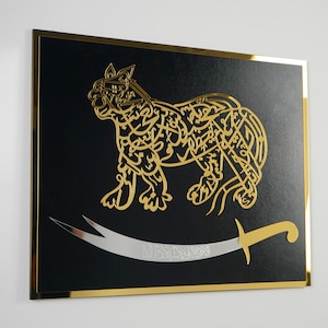 Puede incluir: Una pieza de arte de pared enmarcada en negro con un dise&ntilde;o met&aacute;lico dorado de un le&oacute;n estilizado con una espada. El le&oacute;n est&aacute; hecho de caligraf&iacute;a &aacute;rabe.