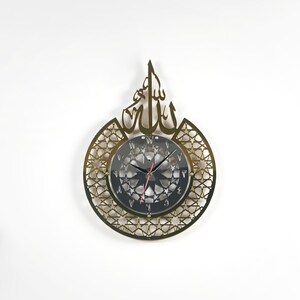 May include: Gold-colored wall clock with a circular, intricate design featuring a star pattern and the Arabic word "Allah" in a decorative font. The clock face is black with white Roman numerals and a silver-colored hour and minute hand.