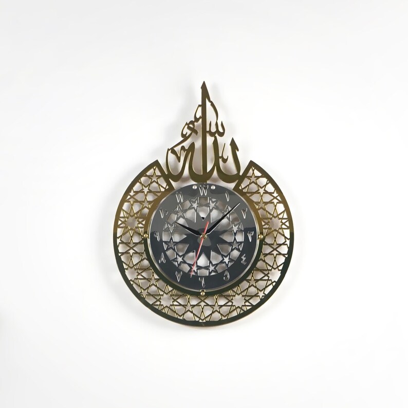 May include: Gold-colored wall clock with a circular, intricate design featuring a star pattern and the Arabic word "Allah" in a decorative font. The clock face is black with white Roman numerals and a silver-colored hour and minute hand.