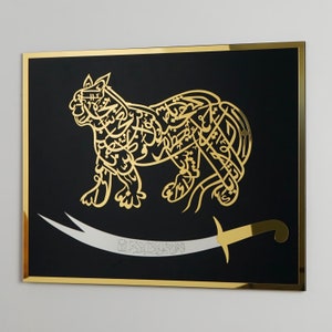 Puede incluir: Una pieza de arte de pared enmarcada en negro con un dise&ntilde;o met&aacute;lico dorado de un le&oacute;n con caligraf&iacute;a &aacute;rabe. El le&oacute;n est&aacute; de pie sobre una espada con un mango dorado.