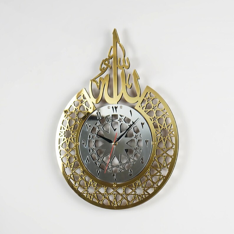 May include: Gold-tone wall clock with a decorative Arabic calligraphy design and a silver clock face with black hands. The clock face features a geometric pattern with stars.