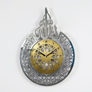 May include: A silver and gold wall clock with an intricate geometric design and Arabic numerals. The clock features the word "Allah" in Arabic script.