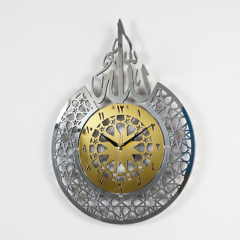 May include: A silver and gold wall clock with an intricate geometric design and Arabic numerals. The clock features the word "Allah" in Arabic script.