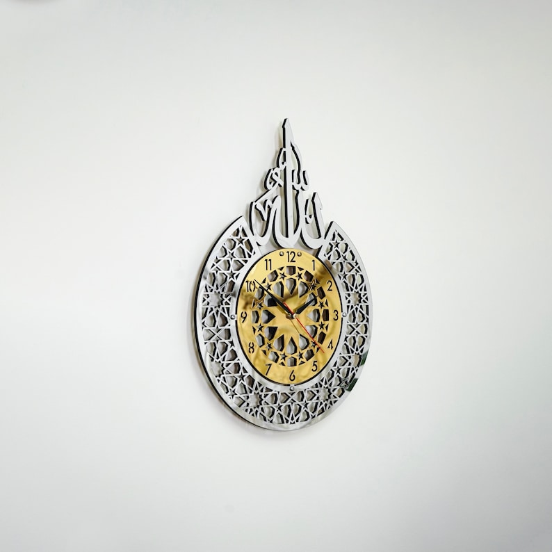 May include: A silver and gold wall clock with an intricate geometric design and the Arabic word "Allah" in the center. The clock face is gold with black numbers and hands.