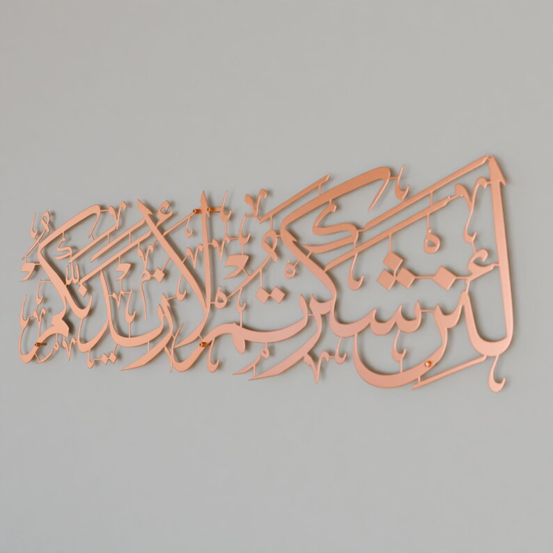 May include: A copper-colored metal wall art piece featuring Arabic calligraphy. The calligraphy is in a traditional style and is arranged in a flowing, decorative pattern.