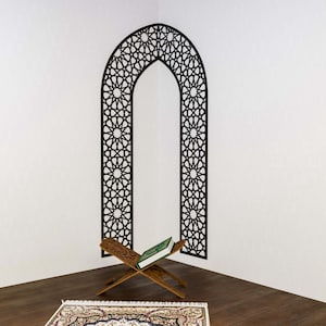 May include: A wooden prayer stand with a green book resting on it, in front of a black and white geometric arch wall decal.
