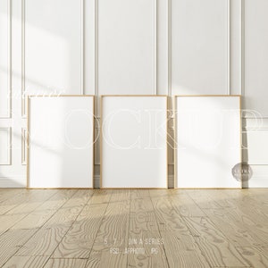 Könnte beinhalten: Drei leere Bilderrahmen mit einem hellen Holzrahmen und weißen Passepartout sind an einer weißen Wand mit dekorativen Leisten angebracht. Die Rahmen sind in einer Reihe angeordnet, wobei der linke Rahmen etwas näher am Betrachter ist. Der Boden ist aus hellem Holz.