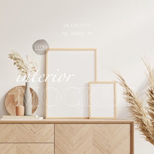 Può includere: Un mobile in legno chiaro con un motivo a spina di pesce sostiene due mockup incorniciati. Un vaso con piante secche e un cestino intrecciato si aggiungono all'arredamento neutro e minimalista. La parola "interior" è visibile.