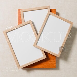 May include: Three wooden picture frames with white interiors are arranged on a textured surface. The frames are angled, with the text "interior MOCKUP" overlaid. The frames rest on an orange wooden block.