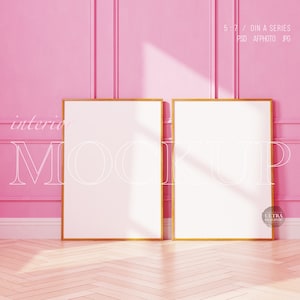 May include: Two gold framed picture frames with white mats are hanging on a pink wall with white trim. The frames are empty and ready for your photos or artwork.  The frames are in a room with a wood floor.