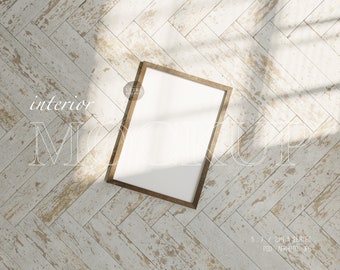 Può includere: Una cornice in legno marrone con un passepartout bianco e una tela bianca vuota all'interno. La cornice è appoggiata su un pavimento in legno sbiancato con un motivo a spina di pesce. Il pavimento è illuminato dalla luce del sole che entra da una finestra.