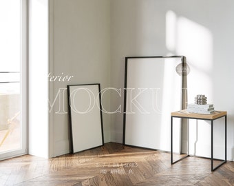 May include: Two black framed empty picture frames, one large and one small, are leaning against a white wall. A small wooden side table with a black metal frame sits in the corner of the room. A small concrete sculpture sits on top of the table.