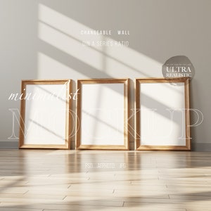 Op de afbeelding: Drie houten fotolijsten met witte passe-partouts en lege witte ruimtes erin. De lijsten staan op een lichte houten vloer met een witte muur erachter. De tekst "CHANGEABLE WALL DIN A SERIES RATIO" staat bovenaan de afbeelding. De tekst "ULTRA REALISTIC" staat in een cirkel rechtsboven in de afbeelding.