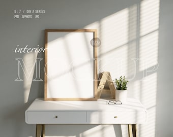 Può includere: Una scrivania bianca con due cassetti e gambe dorate, una cornice in legno con un poster bianco vuoto all'interno, una lettera A in legno e una piccola pianta in vaso sopra la scrivania. La scrivania è davanti a un muro bianco con la luce del sole che entra da una finestra.