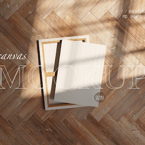 Puede incluir: Una maqueta de lienzo blanco con un marco de madera, que se encuentra sobre un suelo de madera con un patrón de espiga. El lienzo está en blanco y listo para su diseño.
