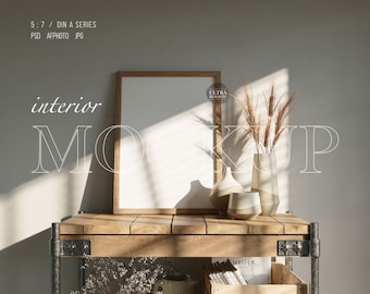 Può includere: Una cornice in legno con un passepartout bianco e una tela bianca vuota all'interno. La cornice è appoggiata su uno scaffale in legno con un vaso di fiori secchi e altri oggetti decorativi. Lo sfondo è una parete di colore grigio chiaro.