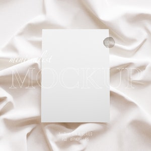 May include: A white card mockup on a white fabric background. The card is blank and has a subtle texture. The fabric is smooth and has a slight sheen. The text "minimalist MOCKUP" is visible in the image.