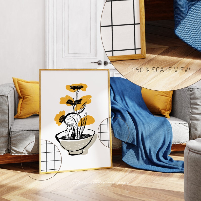 May include: A framed print of a black and white illustration of a yellow flower in a bowl. The print is hanging on a wall in a living room setting with a sofa, throw pillows, and a blanket.