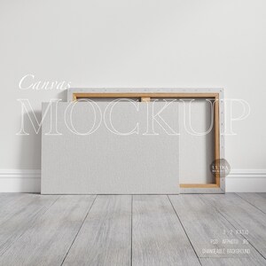 May include: A mockup of a canvas print with a wooden frame. The canvas is a light gray color and the frame is a light brown color. The canvas is leaning against a white wall and the floor is a light gray wood.