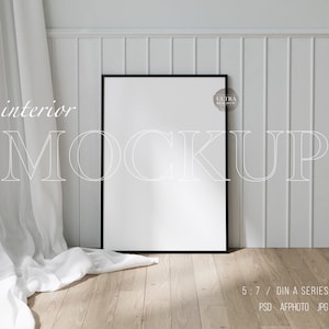 Pode incluir: Uma cortina branca pendurada na frente de uma parede branca com uma maquete de moldura preta. A moldura está em um piso de madeira. O texto "interior mockup" está escrito em branco na parede. O texto "ultra realistic" está escrito em branco em um círculo cinza no canto superior direito da moldura.